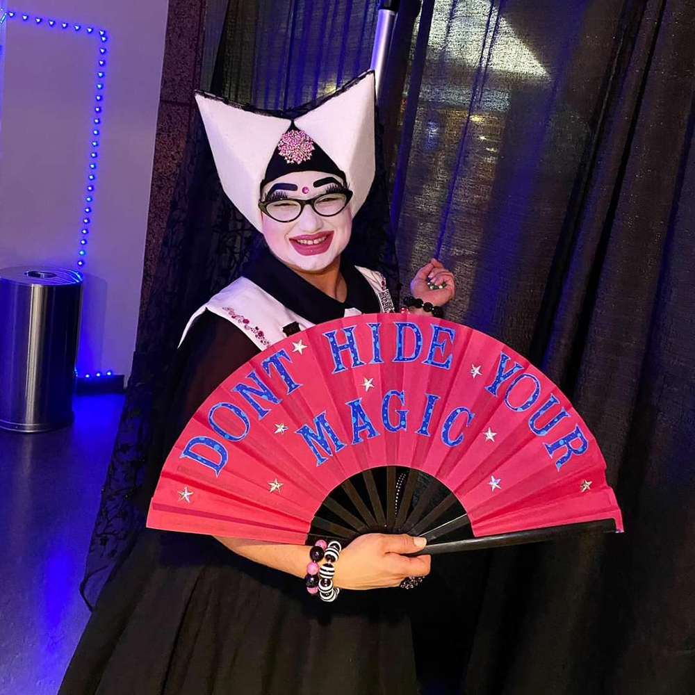 Twinkle Van Winkle holding a fan that says "Don't hide your magic"